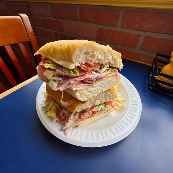 A large, stacked Italian sub sandwich with various meats, cheese, and vegetables on a white plate.