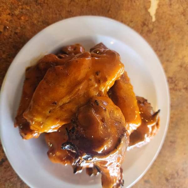 A plate of Dontae's Highland Pizza Parlor's chicken wings coated in a rich, orange sauce.