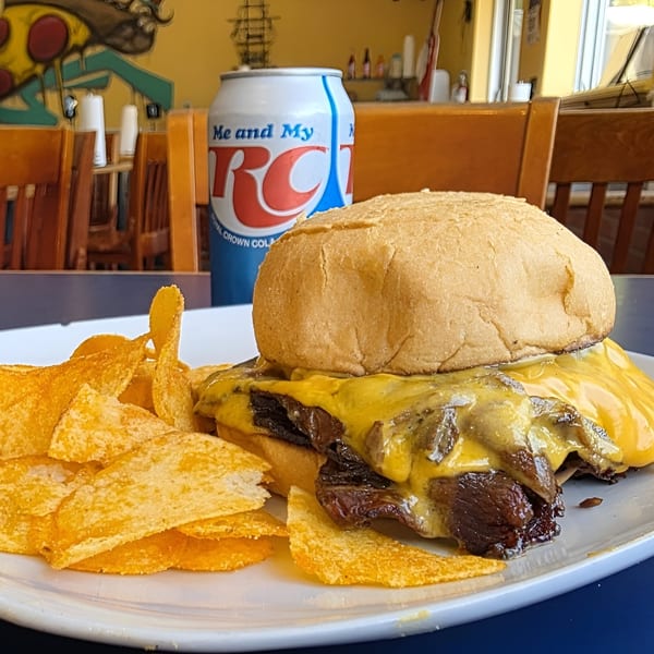 Cheesesteak sandwich with potato chips and an RC Cola can on a table at Dontae's Highland Pizza Parlor.