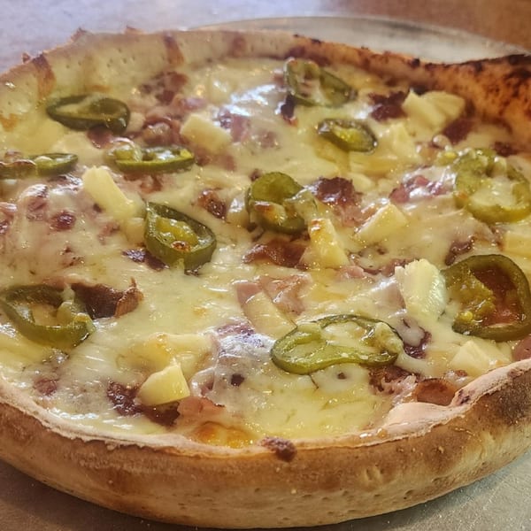 A close-up of a Dontae's Highland Pizza with melted cheese, pineapple, bacon, and jalapeños.